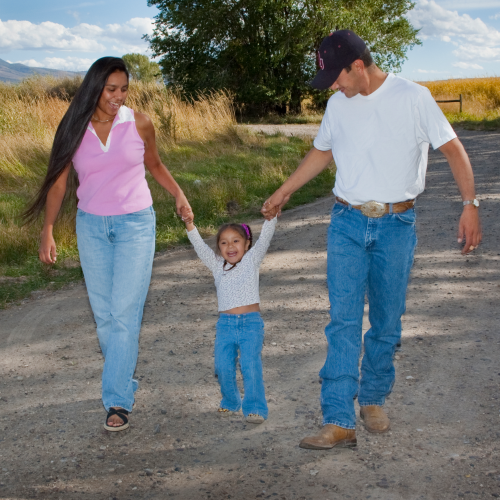 Native family swinging their child as walking down a dirt road.
